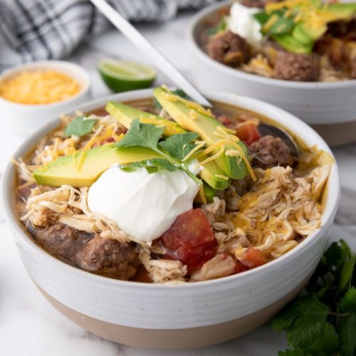 A bowl of taco soup with a side of shredded cheese.